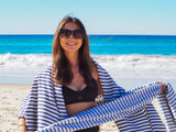 PORTSEA TURKISH COTTON TOWEL - DENIM being held by a mwoman on the beach